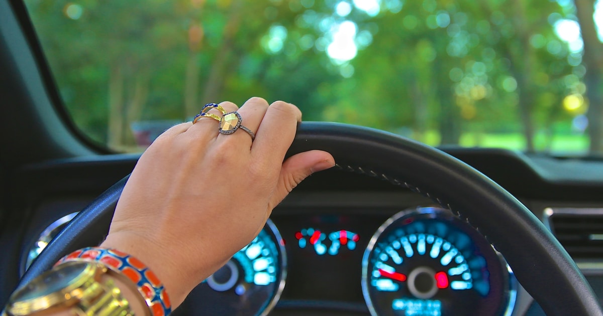 Hand with rings holding top of steering wheel