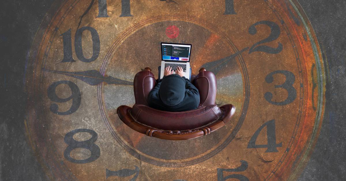 Person in chair on laptop with large clock in background