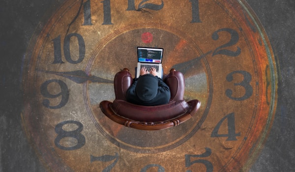 Persona en silla en portátil con gran reloj en segundo plano